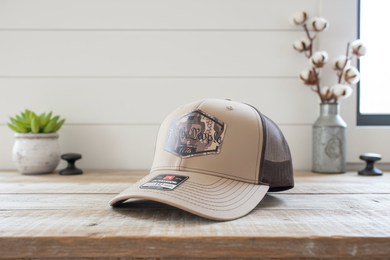 Beige trucker hat with 'We the People' and Richardson logo on a reflective surface.